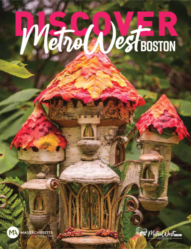 A whimsical fairy house with red and orange leaf-like roofs sits among lush green plants. The text reads, Discover MetroWest Boston with our Visitors Guide. Logos for Massachusetts and MetroWest Visitor’s Bureau are visible.