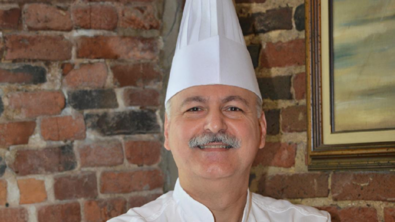 A smiling chef with a white mustache