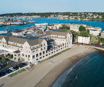 An above shot of the Beauport Hotel, in Gloucester, Massachusetts, overlooking a sandy beach and blue ocean water.
