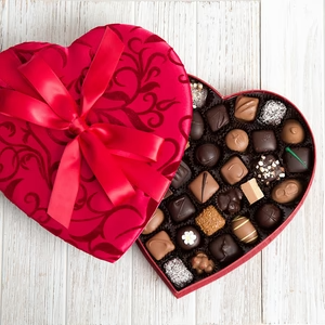 An open red heart-shaped box of assorted chocolates against a wooden white background from Hilliards Chocolates.