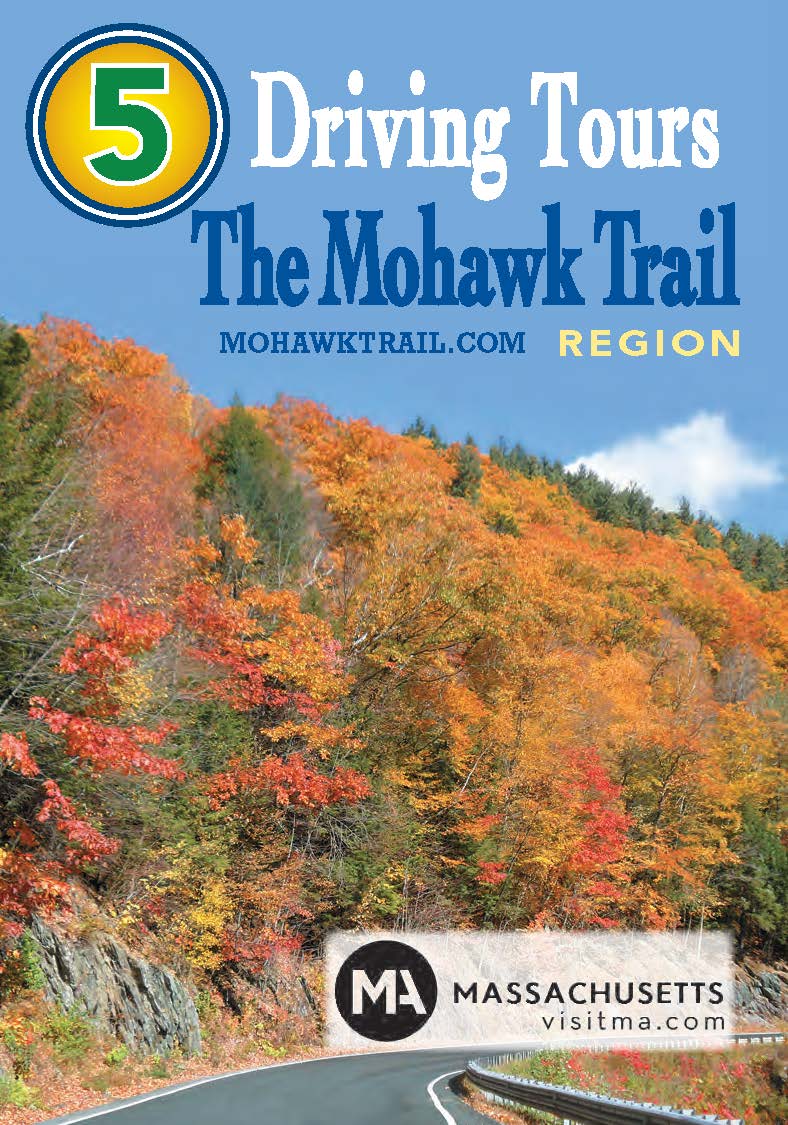 Scenic road curving through a forest of vibrant autumn foliage with a sign promoting “5 Mohawk Trail Driving Tours” and “Massachusetts VisitMA.com” at the bottom.