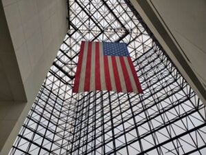 A large American flag hangs high above the geometric glass pavilion in the John F. Kennedy Presidential Library and Museum in Boston, Massachusetts.