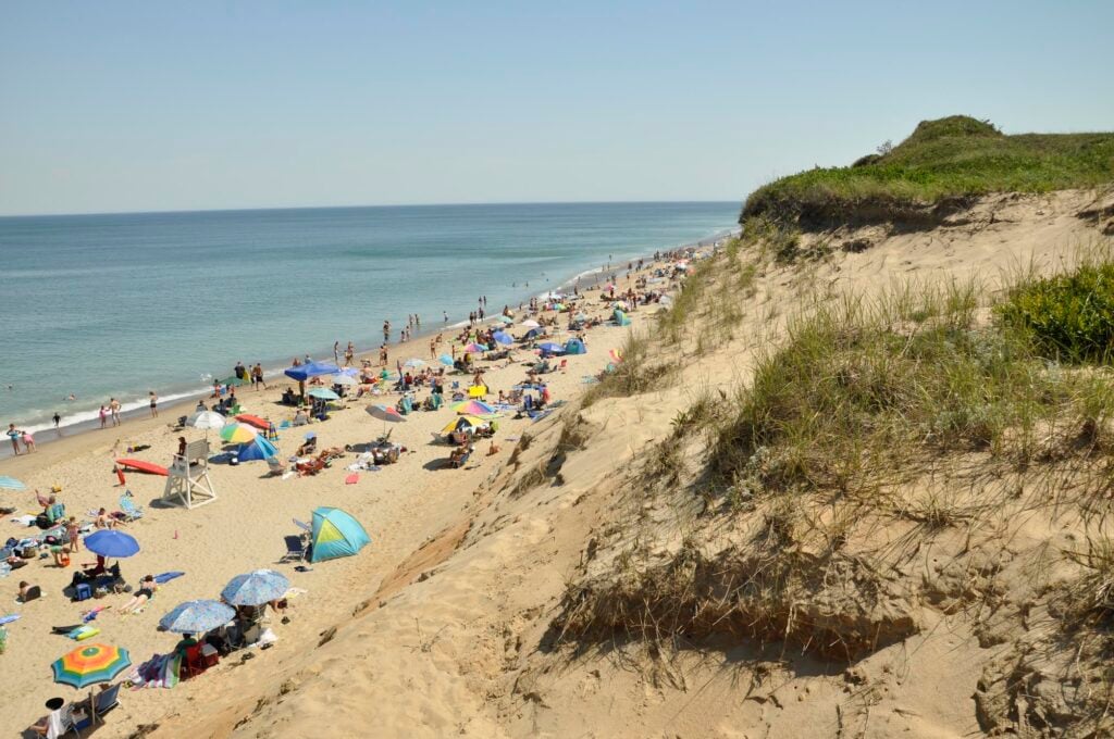 Beachgoers line up against a sandy cliff.