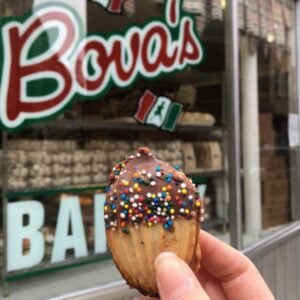 Italian cookie with frosting and sprinkles in front of a shop window that says Bova's Bakery