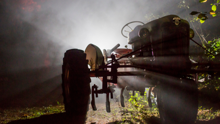 A spotlight illuminates an old tractor at night.