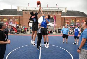 Two kids, one wearing black and one wearing blue, jump for a basketball during a game at the National Basketball Hall of Fame in Springfield, Massachusetts.