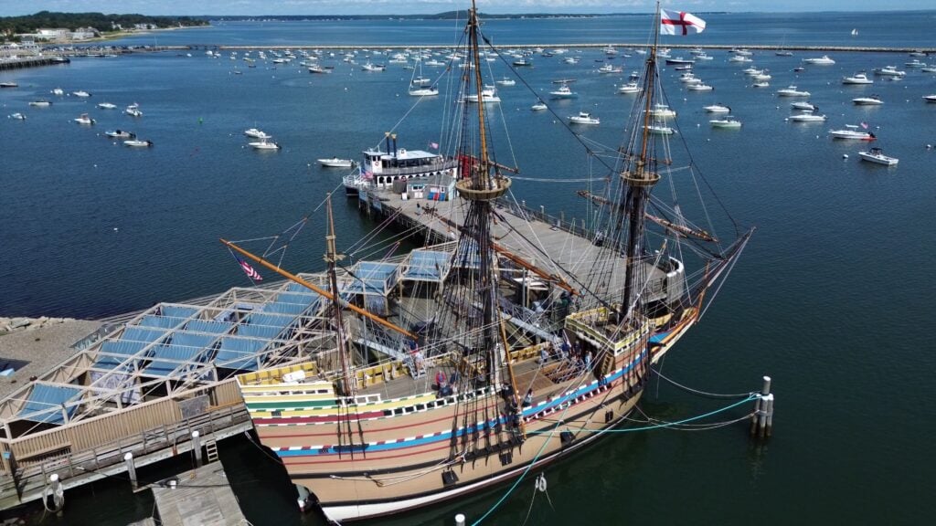 The replica Mayflower II boat sits in a harbor flanked by smaller boats in Plymouth, Massachusetts.