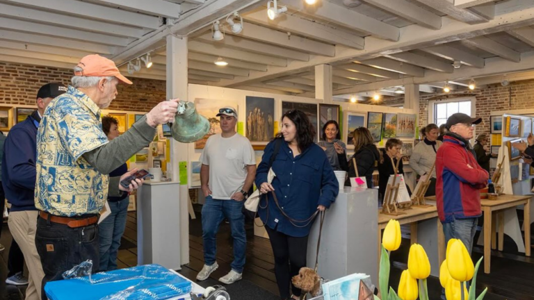 An artist discusses their work amongst a crowd in a gallery.