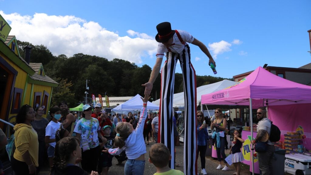 A person on stilts bends down to give a high five at a festival.
