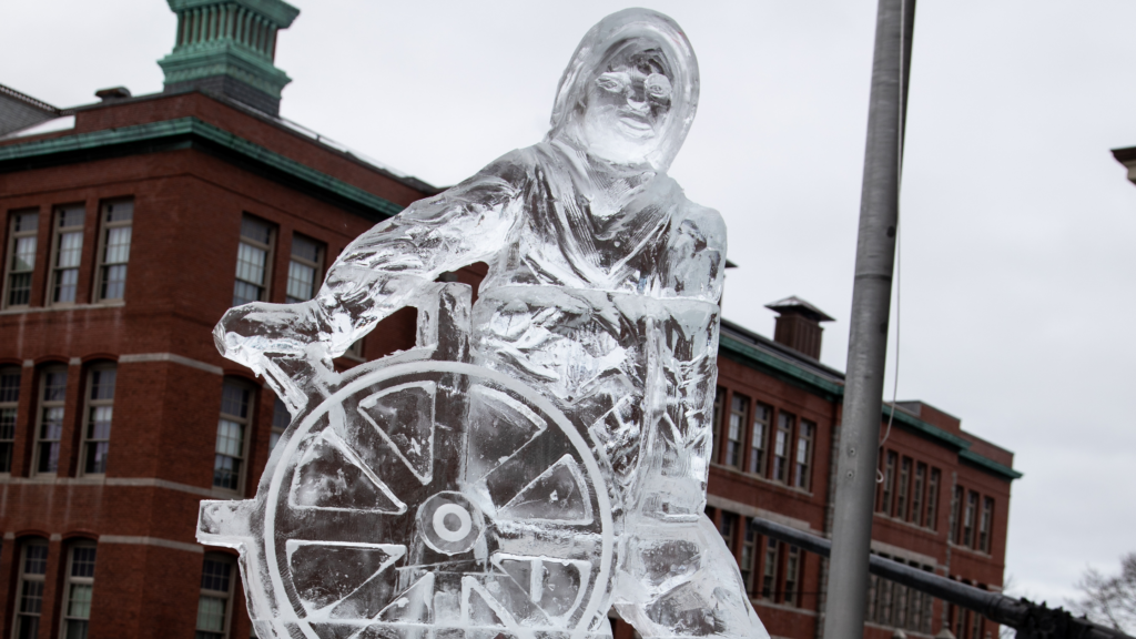 A ice sculpture of Gloucester's The Man at the Wheel statue - a sailor navigating a round wooden ship steering wheel.