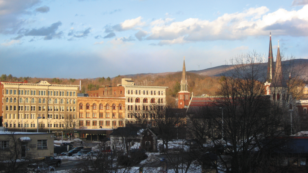The skyline of the town of North Adams, Massachusetts - quaint brick buildings illuminated by a bright sun against a clear blue sky.