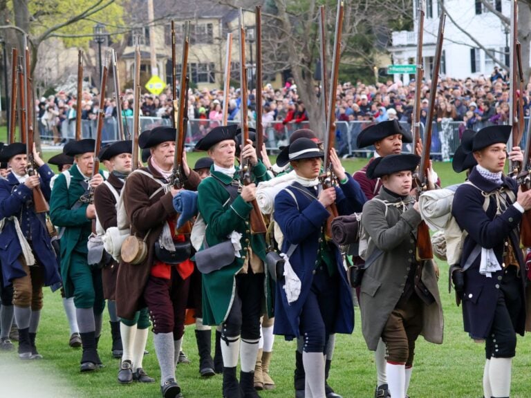 American Revolution Reenactors in Lexington, Massachsuetts line up dressed in period clothing holding muskets.