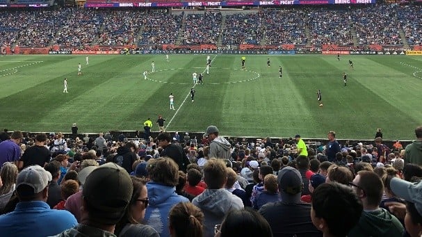 A soccer game takes place on a field in front of hundreds of spectators.