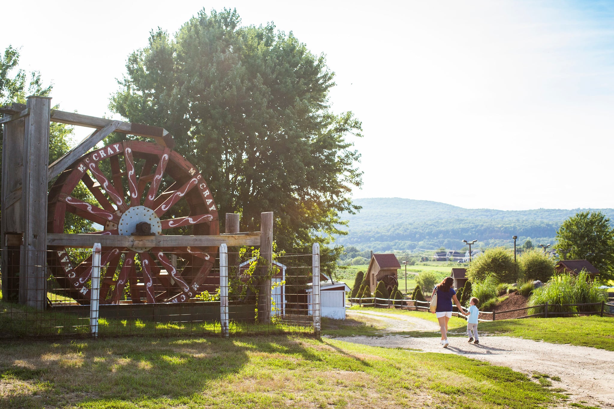 A family walks around a path next to a large water wheel on a sunny day.
