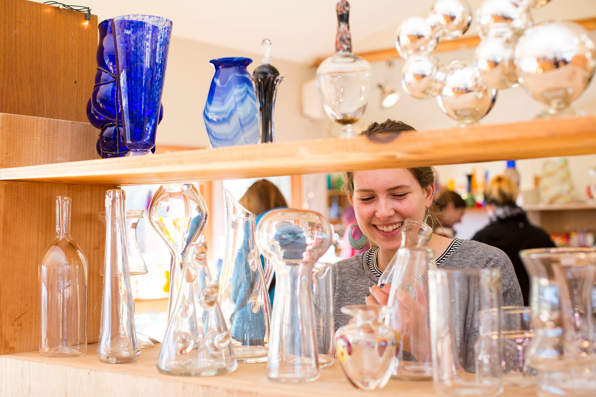 A woman admires glassware for purchase on a shelf.