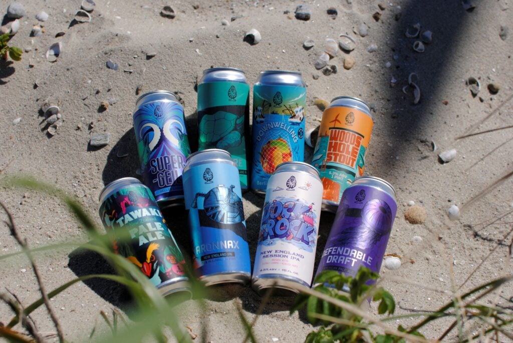 Cans of beer from Aquatic Brewing on a sandy beach.