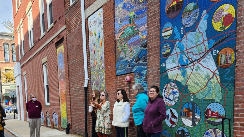 A group of women stand in front of a mural on a brick building.