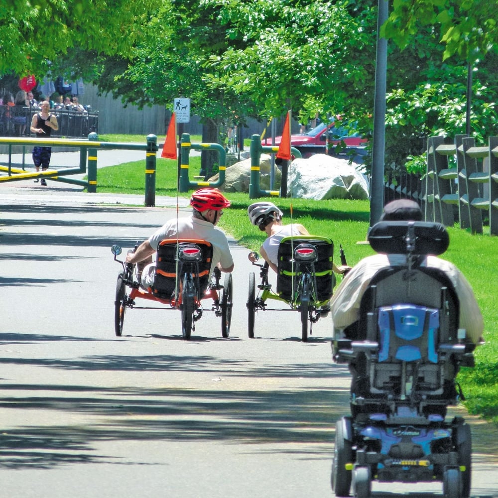 People ride down a bike trail on wheelchairs.