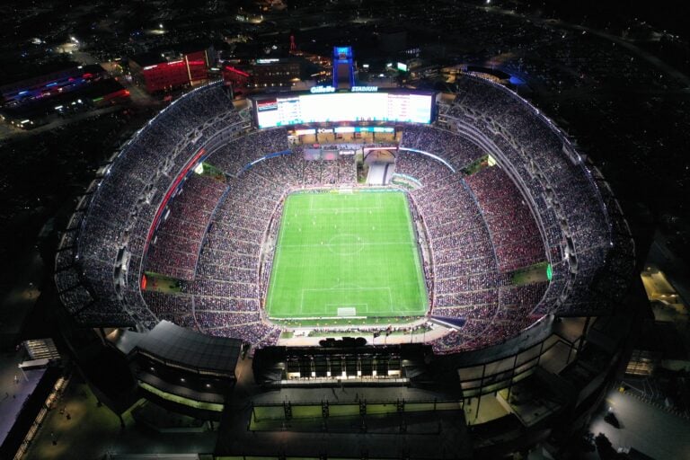 Aerial view of a brightly lit football stadium in Massachusetts, packed with spectators enjoying live soccer at night.