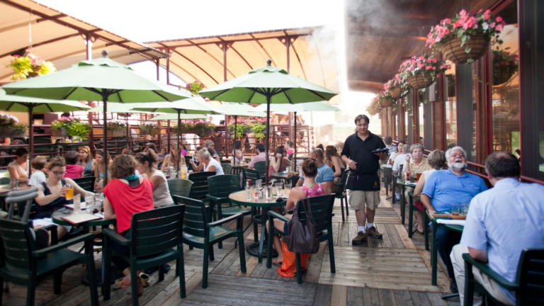 Many people sit on the outdoor patio of a restaurant enjoying their meals.