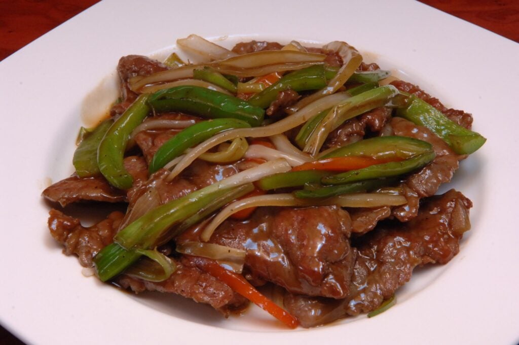 A white plate full of steak, cooked peppers, and noodles.