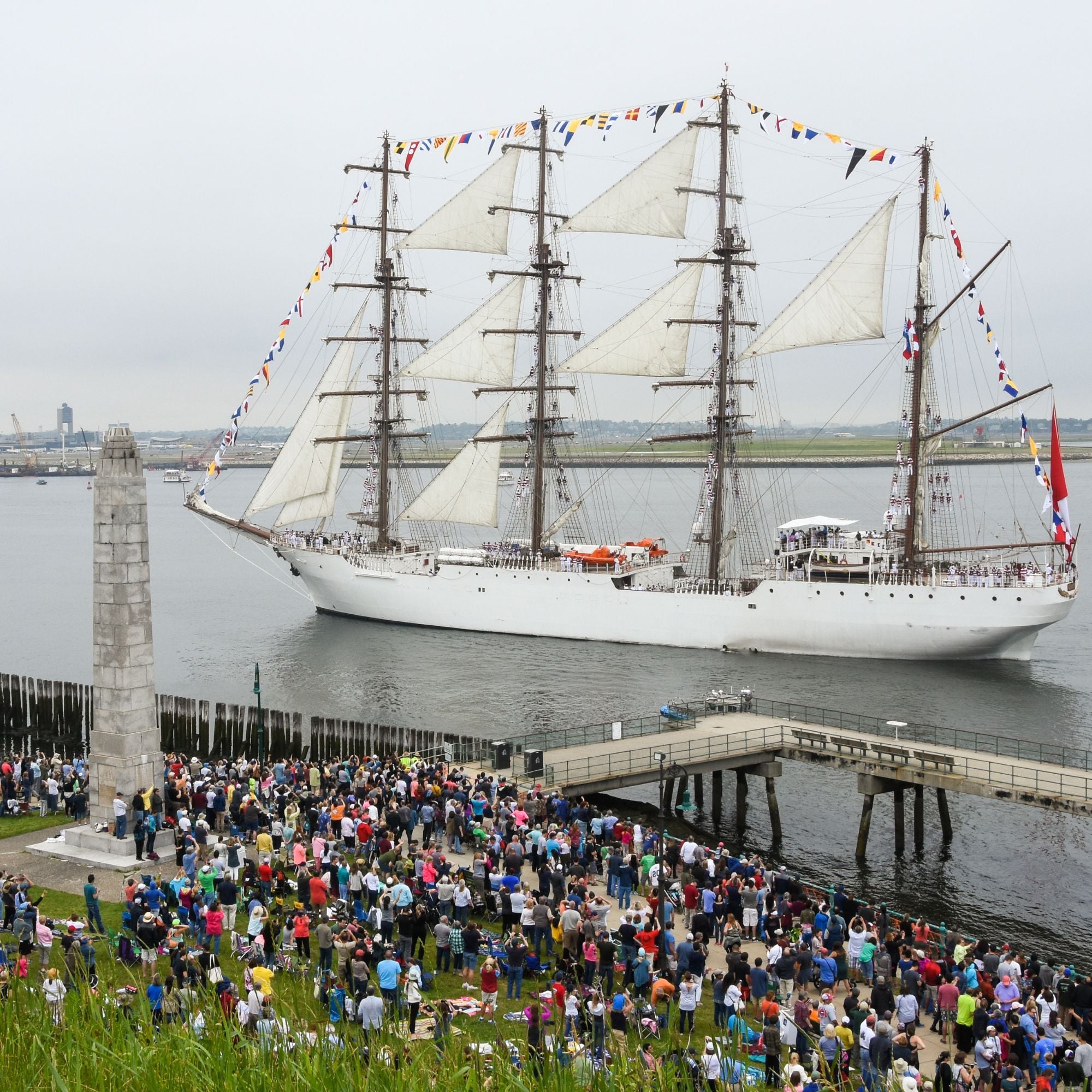 People crowd to watch a large wooden ship adorned with colorful flags.