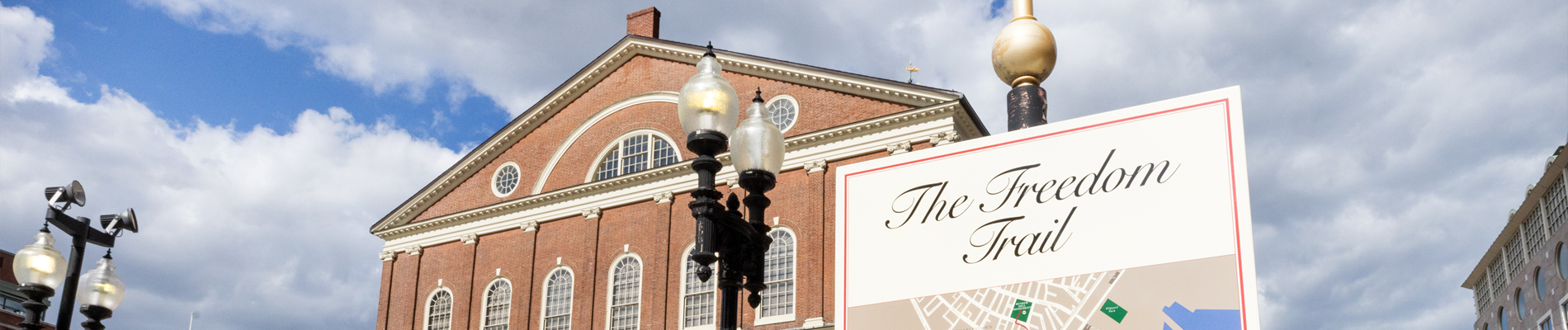 A sign for the Freedom Trail in Boston in front of a brick building, Faneuil Hall.