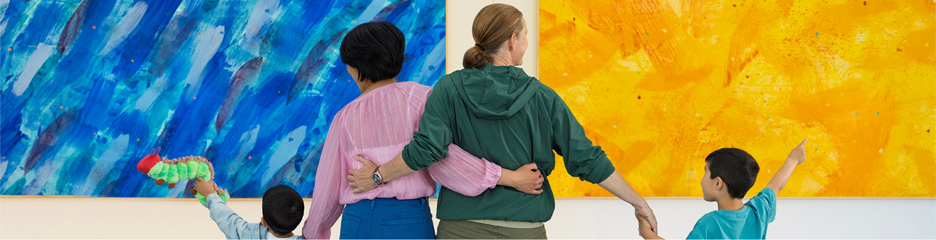 Four people, two adults and two children, stand with their backs to the camera admiring colorful abstract paintings in a Massachusetts art gallery—a welcoming destination for LGBTQ+ travel and family experiences.