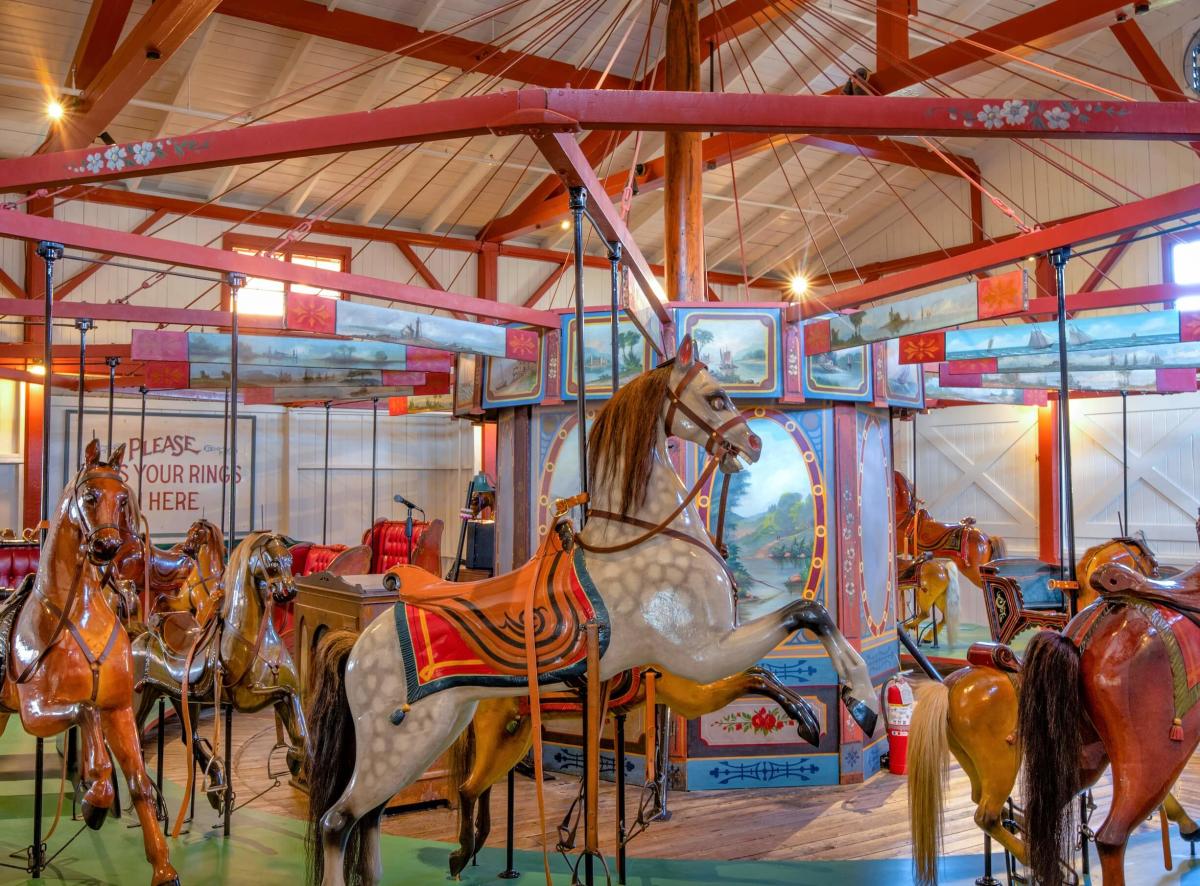 A vintage carousel featuring ornate, hand-painted wooden horses with decorative saddles inside a brightly lit, red and white pavilion—one of the most charming and inexpensive things to do in Massachusetts.