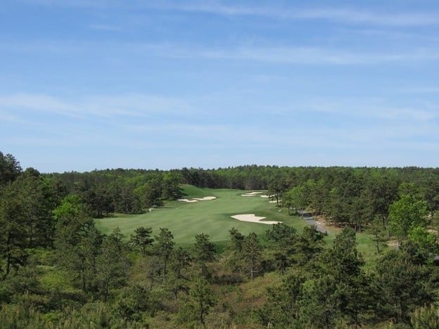 A golf course fairway with sand bunkers, surrounded by green trees under a blue sky with wispy clouds—a picturesque scene typical of unique golf courses in Massachusetts. If you're ready to hit the links, this is an inviting destination.